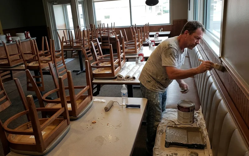 Restaurant dining room after close with chairs stacked and a painter at work