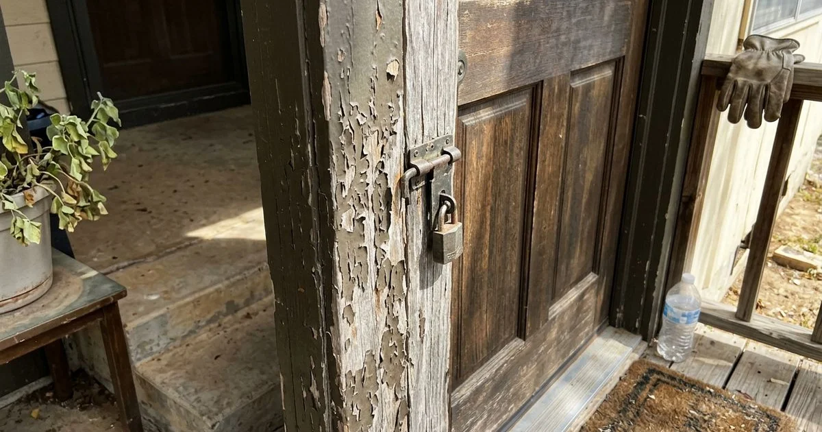 Blistered dark paint on a sun-baked exterior door frame in harsh midday light